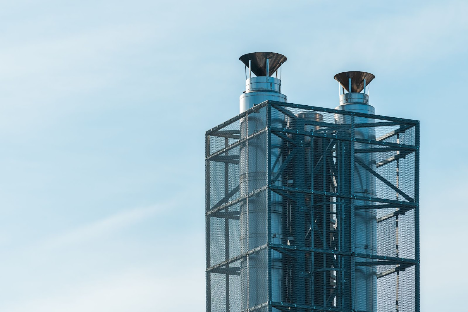 Tall industrial heat exchangers with a metal mesh frame against a clear sky, used in environmental flue gas treatment.